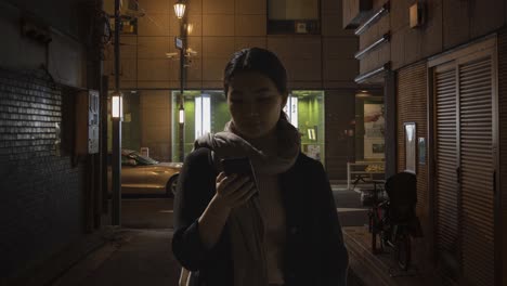 Woman-Walking-Along-Dark-City-Street-At-Night-Using-Mobile-Phone